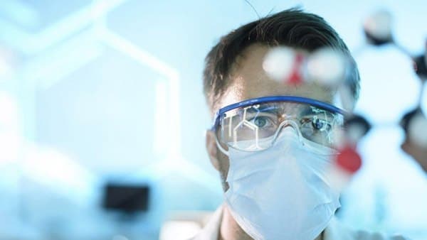 A scientist in protective goggles and mask in a laboratory