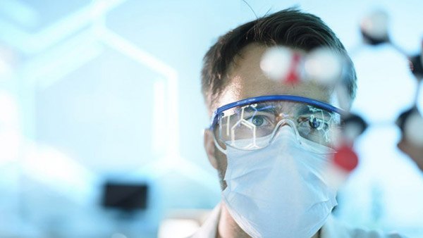 A scientist in protective goggles and mask in a laboratory