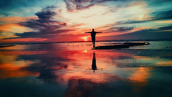A person with arms outstretched at a colorful sunset