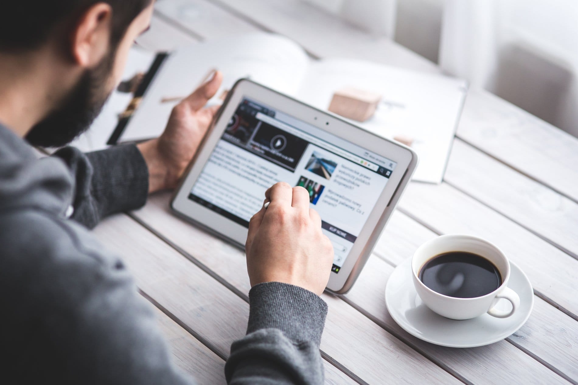 A person reading the news on a tablet with a cup of coffee
